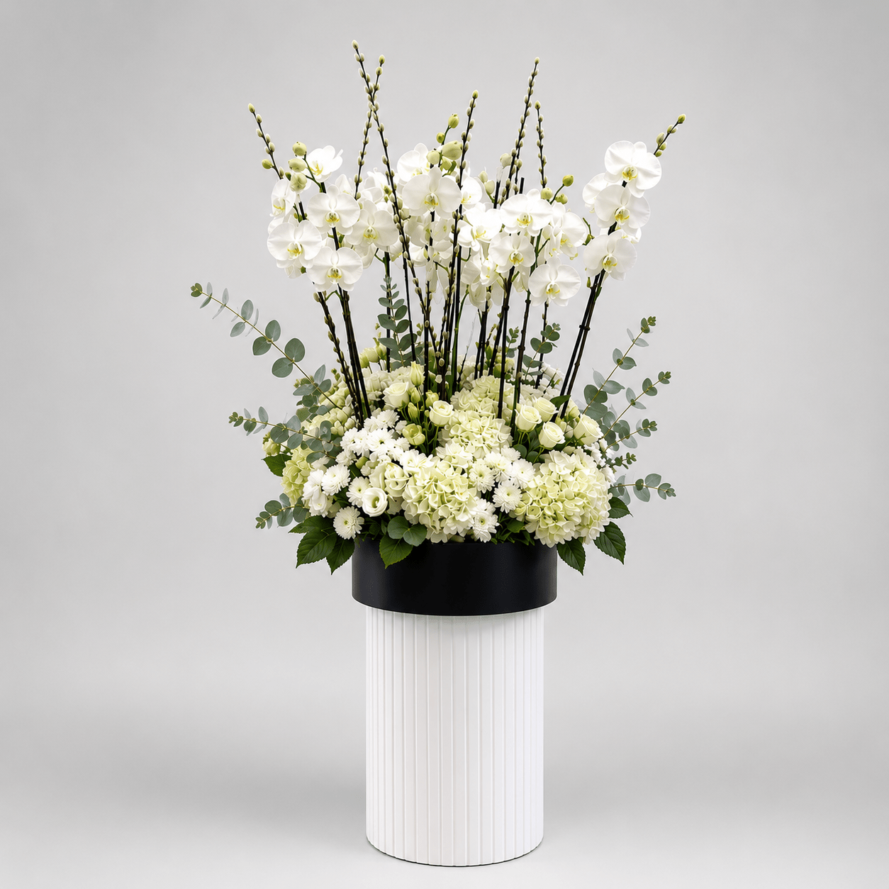 Floral arrangement in a black pot on a white vase against a gray background-White Orchid & Hydrangea Luxury Arrangement