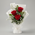 A bouquet of three red roses with green leaves and white baby's breath flowers, wrapped in white paper and tied with a white ribbon, set against a solid gray background.