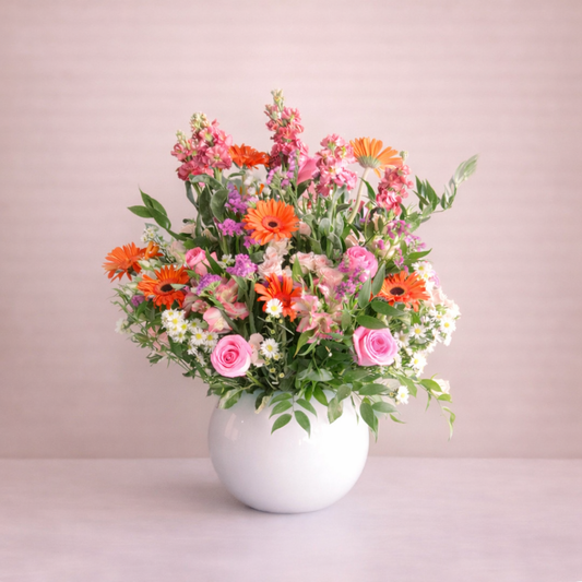 Bouquet of colorful flowers in a white vase on a light pink background