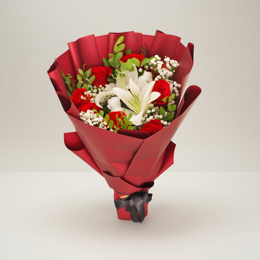 A red rose flower bouquet with lilies, wrapped in red paper with a black ribbon.
