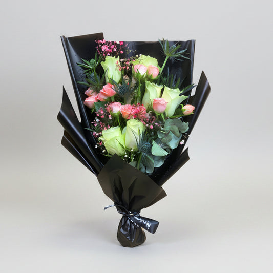 A bouquet of white flowers including shades of pink and green, wrapped in black paper with a black ribbon.