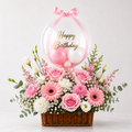 pink birthday flower basket with roses, hydrangeas and astilbe in a woven cane basket topped with a clear bubble balloon filled with mini pink balloons and a gold Happy Birthday message.