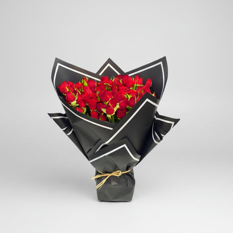 Bouquet of red roses wrapped in black paper with a gold ribbon on a white background