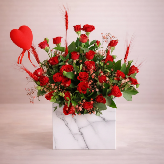 Bouquet of red roses with a heart-shaped gift on a marble base against a light background