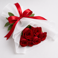 A bouquet of red roses wrapped in sheer white tissue paper and tied with a large red satin bow, photographed on a clean white background.