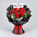 A bouquet of 14 red roses wrapped in black paper with a red ribbon and a small card that reads 'you & me FOREVER & ALWAYS', photographed on a light gray background.