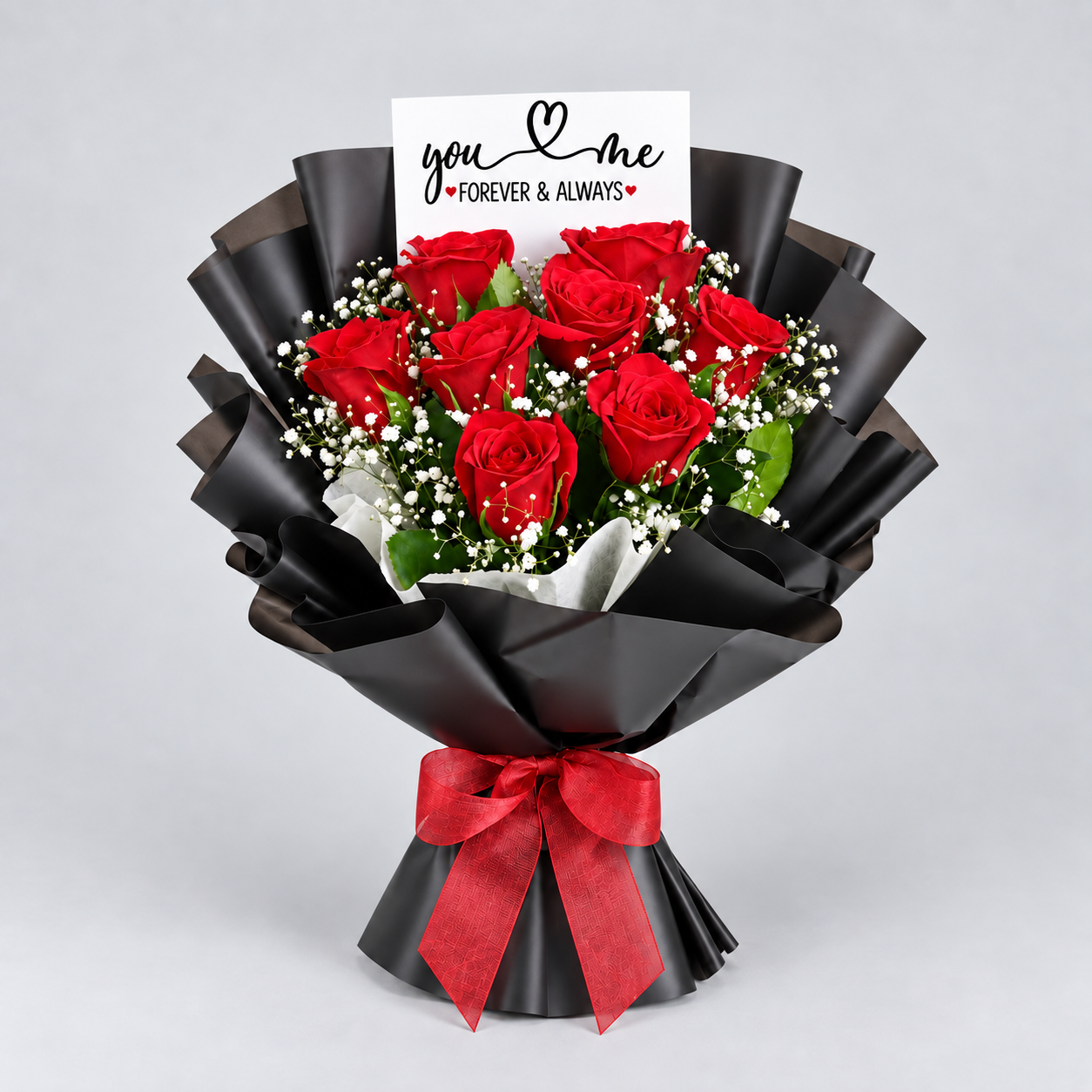 A bouquet of 14 red roses wrapped in black paper with a red ribbon and a small card that reads 'you & me FOREVER & ALWAYS', photographed on a light gray background.