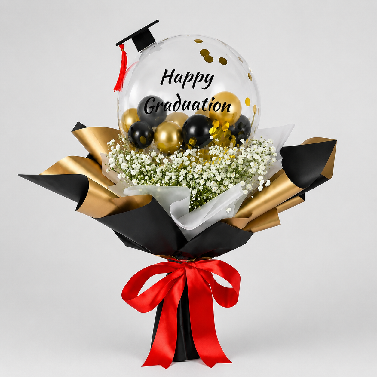 Graduation-themed balloon bouquet with a transparent balloon featuring 'Happy Graduation' text, surrounded by gold and black balloons, and white flowers on a light gray background.