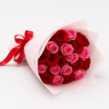 A bouquet of red and pink roses wrapped in light pink tissue paper with a red ribbon tied at the left side, photographed on a clean white background.