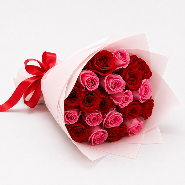A bouquet of red and pink roses wrapped in light pink tissue paper with a red ribbon tied at the left side, photographed on a clean white background.