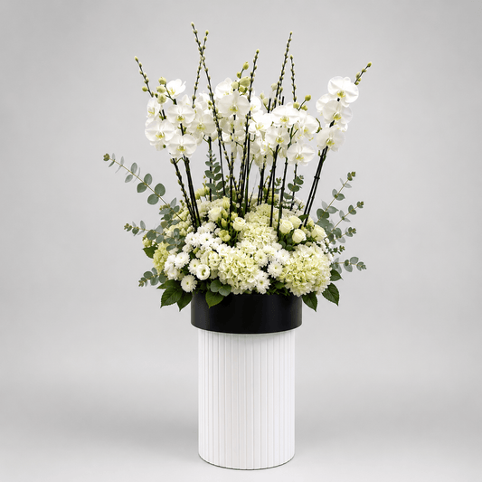 Floral arrangement in a black pot on a white vase against a gray background-White Orchid & Hydrangea Luxury Arrangement